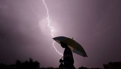 Un peatón camina con un paraguas durante una tormenta eléctrica por la noche en Jammu (India).