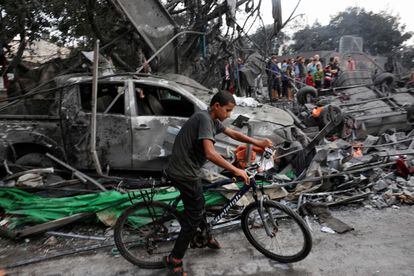 Un joven circula con su bicicleta mientras civiles, al fondo, buscan supervivientes de un edificio afectado por ataques israelíes en Rafah, en el sur de la franja de Gaza.