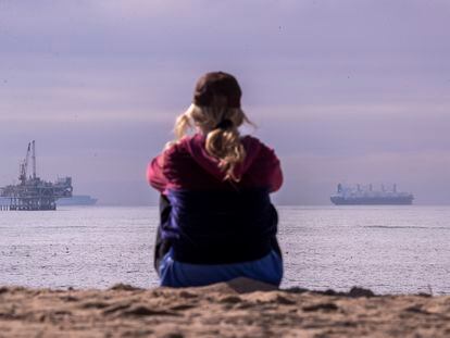 Una mujer mira hacia el océano en California; al fondo, una plataforma petrolífera y un buque.