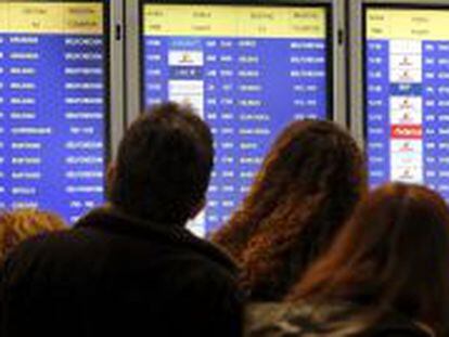 Varias personas consultan en un panel informativo el estado de sus vuelos, en la T-4 del aeropuerto Adolfo Su&aacute;rez Madrid-Barajas.