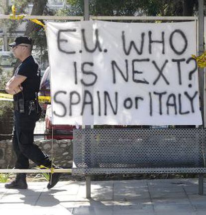 Un policía ante una pancarta en la que se puede leer "Unión Europea, ¿Quién es el siguiente? España o Italia" frente al Parlamento en Nicosia