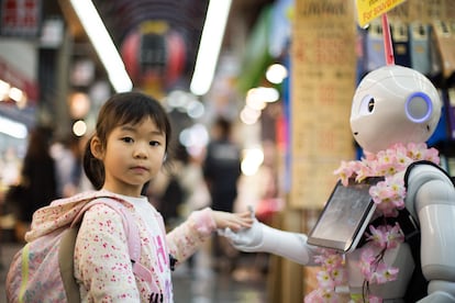 Una niña acompañada de un robot en un mercado de Osaka, en Japón.