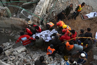 Un grupo de bomberos, con equipamiento de desescombro, transporta un cuerpo que había quedado sepultado, tras la explosión en la mezquita paquistaní de este lunes.