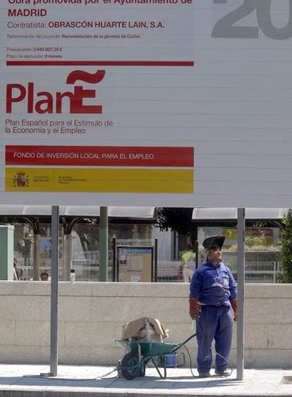 Un trabajador de la construcción, ante un cartel del Plan E situado en una obra de Madrid.