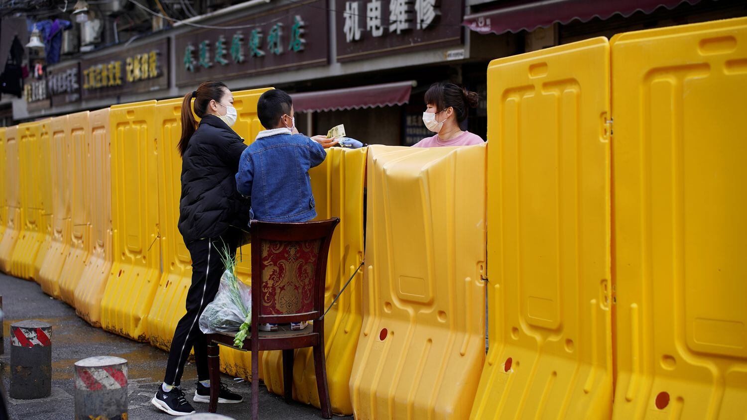 Una mujer paga la compra de un mercadillo delimitado por una barrera levantada durante la cuarentena, en Wuhan.