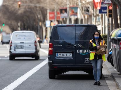 Una repartidora de Amazon carga con varios paquetes mientras tiene la furgoneta en el carril bus de Travessera de les Corts, en Barcelona.