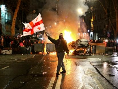 Un hombre alza la bandera de Georgia ante una barricada levantada con un coche destruido frente al Parlamento en la noche del 8 al 9 de marzo.