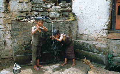 Dos niños se bañan con el agua de una fuente para beber en Bután.