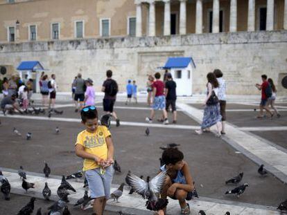 Un grupo de ni&ntilde;os juega con las palomas frente al edificio del Parlamento griego en Atenas
