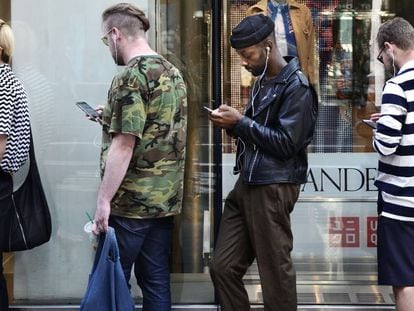 Tres jóvenes usan sus móviles mientras hacen cola para entrar en un establecimiento Uniqlo, en Nueva York.
