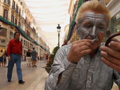 Un mimo se maquilla para actuar en la calle Larios de M&aacute;laga.
