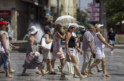Un grupo de turistas se protegen del intenso sol con sombreros o paraguas mientras caminan por la plaza de la Virgen, en Valencia, el lunes.