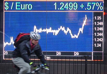 Un ciclista pasa por delante de un tablero en Londres que muestra un momento de la cotización de ayer del euro frente al dólar.