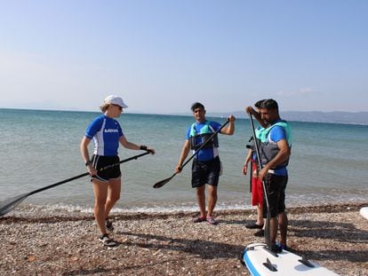 La instructora (izquierda) explica a los tres refugiados cómo manejar el pádel, en la playa de Skala Oropou, al norte de Atenas.
