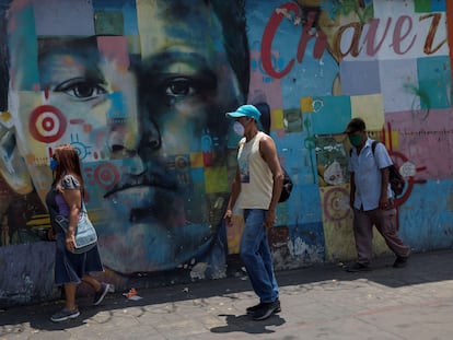 Tres personas con tapabocas caminan frente a un mural de Hugo Chávez, el 3 de marzo en Caracas, Venezuela.