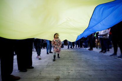Una niña pasa por debajo de la bandera de Ucrania, durante una protesta en Tirana, Albania, contra la invasión Rusa.