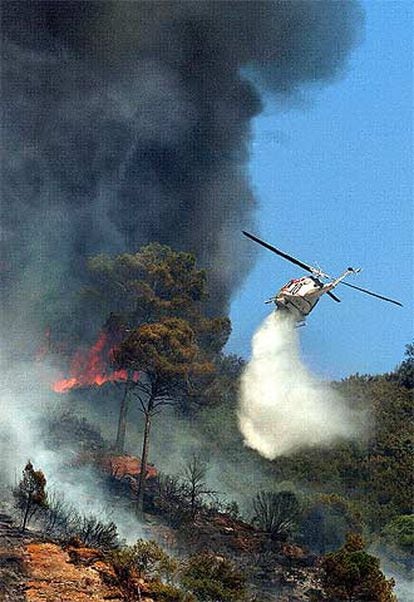 Un helicóptero vierte agua sobre las llamas durante las labores de extinción del incendio junto a la autopista AP-, en Martorell.