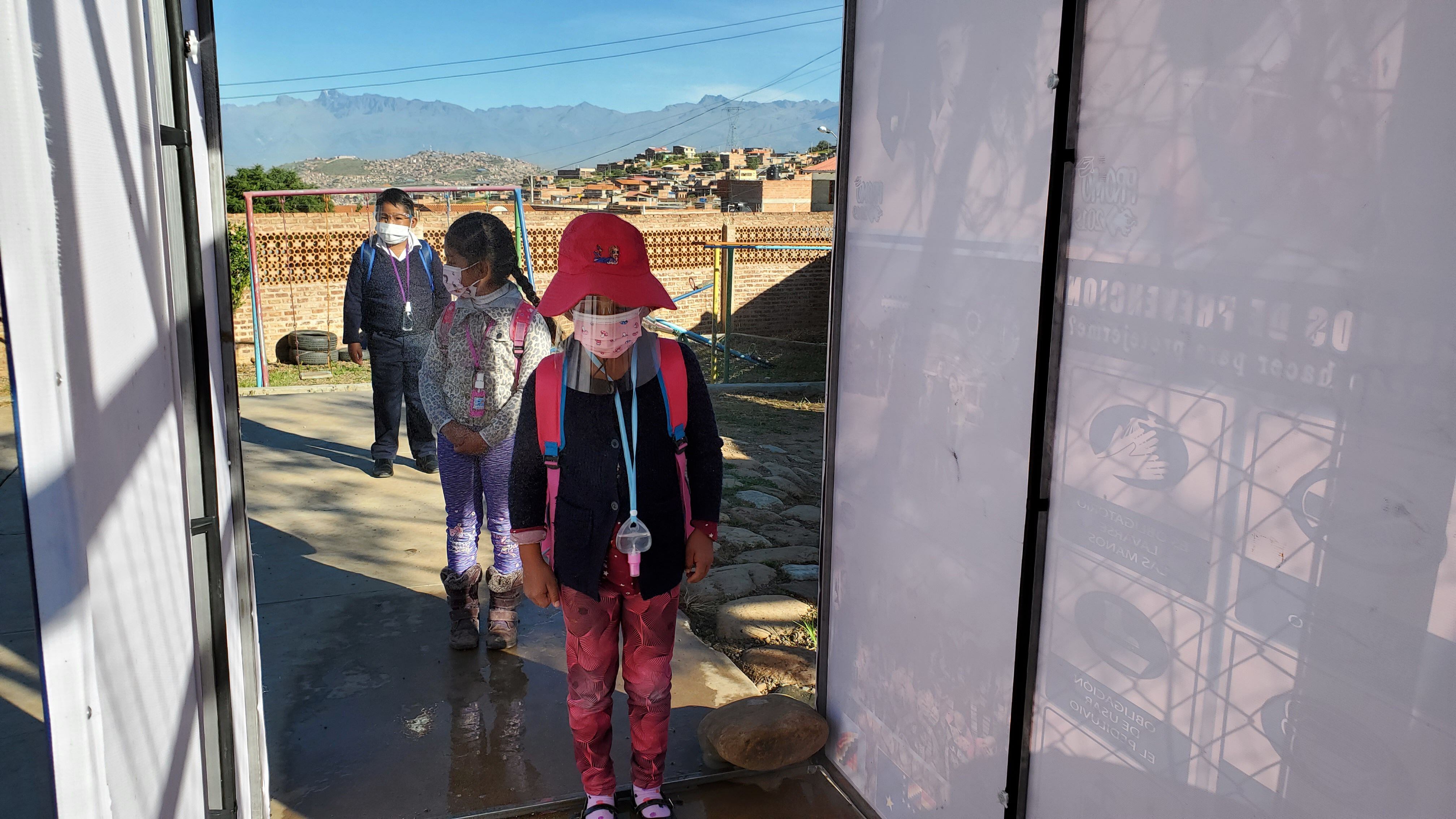 Estudiantes de primaria de la Unidad Educativa San Andrés, en Cochabamba, Bolivia, pasan por la cámara de desinfección antes de ingresar a las aulas para pasar clases.