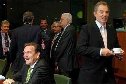 El primer ministro británico, Tony Blair, con una taza de té en las manos, pasa por detrás del canciller alemán, Gerhard Schröder.
