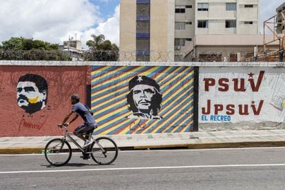A man passes on his bicycle in front of a mural with the image of the President of Venezuela, Nicolás Maduro, and Ernesto 