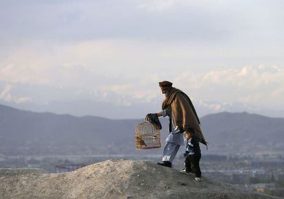 Un hombre sujeta a un niño de la mano mientras camina con una jaula de codornices por una colina de Kabul (Afganistán).