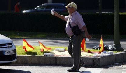 Un hombre ofrece kleenex a los conductores entre banderitas espa&ntilde;olas en el paseo de la Castellana.