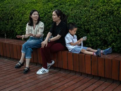 Un niño mira un teléfono móvil mientras dos mujeres conversan junto al río Liangma, el 7 de junio de 2023 en Pekín, China.