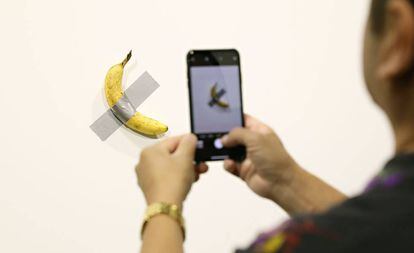 Un visitante saca una foto del plátano adherido a la pared, del artista Maurizio Cattelan.