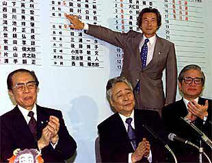 Koizumi señala un tablón con los resultados electorales. En primer plano, los líderes de su partido.