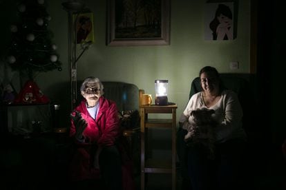 Two women illuminate the living room of their house with flashlights, in Barcelona in 2020.