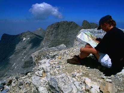 Un montañero descansa en la cima Skolio del monte Olimpo (Grecia), con las cumbres Stefani y Mytikas al fondo.