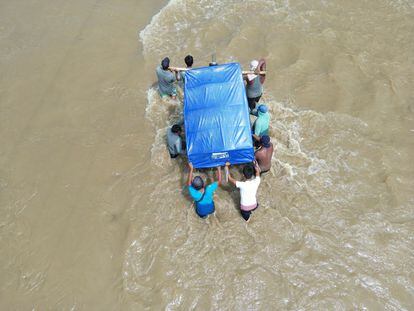 Un mototaxi es llevado en medio de las aguas por ocho hombres. Se trata de una herramienta de trabajo que, al perderse, puede hundir más la vida de algunas familias.