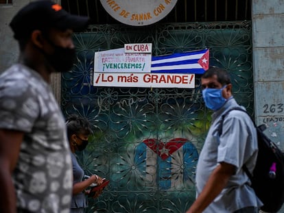 Varias personas caminan frente a una bandera de Cuba, en La Habana