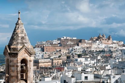 Las blancas murallas aragonesas de Ostuni brillan a lo lejos, casi cegadoras, y demuestran que el blanco no está desprovisto de color, sino todo lo contrario. Una serie de subidas sinuosas con peldaños aquí y allá conducen a callejones cada vez más estrechos. Sin embargo, los espacios angostos a menudo dan paso a inesperadas placitas donde apetece detenerse un instante a escuchar el sonido del viento que sopla desde la campiña italiana. Es casi imposible no enamorarse perdidamente de esta villa, sobre todo desde las murallas. Desde el tramo que aún permanece en pie, la mirada abarca los olivares de los alrededores y el mar cercano que se difumina en el horizonte; luego, uno se da la vuelta instintivamente hacia el pueblo, que parece una nube de polvo blanco casi irreal.
Hay que estar atentos, entre tantos buscadores de selfis, visitantes despistados e incluso alguna estrella de Hollywood. Pese a los turistas, merece la pena visitar el casco antiguo, que se extiende sobre un cerro con las calles dispuestas en círculos concéntricos. Lo mejor es dejarse guiar por el instinto en busca de arcos, escaleras y muros ciegos. En la Piazza della Libertà se encuentran la parte antigua y la nueva, y allí están el Ayuntamiento, un monasterio franciscano y, muy cerca, el neoclásico Palazzo Zevallos. Pero las obras maestras de la ciudad son la concatedral, la basílica di Santa Maria Assunta y las murallas aragonesas, que se pueden contemplar desde arriba entre los bastiones de Via Stefano Trinchera y, desde abajo, caminando por Viale Oronzo Quaranta.