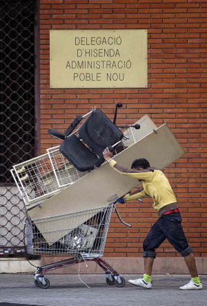 Un hombre acarrea un carrito con chatarra en el Poblenou.