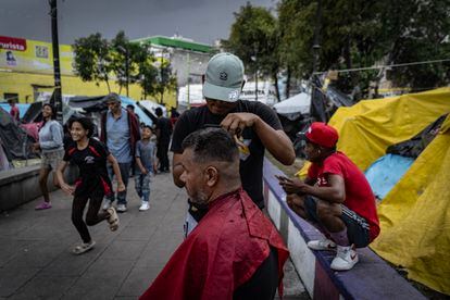 Un migrante corta el pelo a otro, en una barbería montada en el campamento a las afueras de la parroquia. 