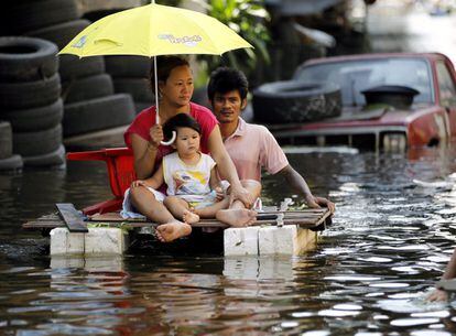 Un hombre transporta a su mujer y a su hija en una barca artesanal mientras abandonan una zona residencial inundada en las afueras de Bangkok