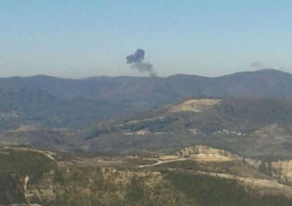 Una columna de fum s'aixeca sobre el perfil de la carena de muntanyes on ha caigut l'aparell rus abatut per caces turcs a la frontera amb Síria.