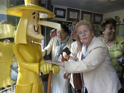 Una mujer toca las manos del muñeco que da nombre a la administración de lotería de Sort, La Bruixa d'Or (Lleida).
