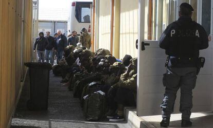 Inmigrantes vigilados por agentes esperan a que varios autobuses los trasladen desde el &#039;hotspot&#039; de Pozzallo (Sicilia) a otros centros de acogida en Italia.