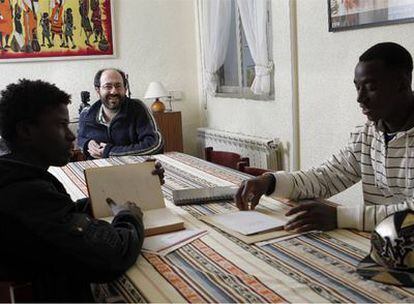 Daniel Izuzquiza y dos de los inmigrantes con los que vive, en el comedor de su casa.