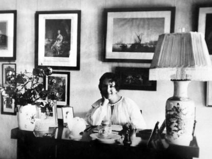 La escritora danesa Karen Blixen posa para la foto apoyada en una mesa de retratos y un jarrón con flores.