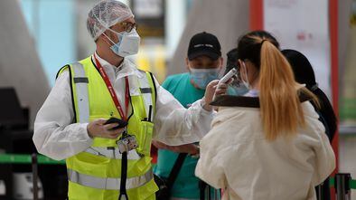 An employee in full protective gear checks the temperature of passengers arriving to check in for their flight bound for Beijing at the Barajas airport in Madrid on June 20, 2020, a day before the country's state of emergency ends following a national lockdown to stop the spread of the novel coronavirus. - With Spain's epidemic now well under control, the government has been cautiously easing out of its mid-March lockdown with travel restrictions soon to be lifted as well. (Photo by PIERRE-PHILIPPE MARCOU / AFP)