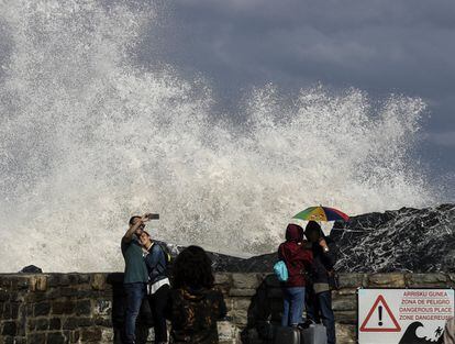 Varias personas toman fotografías y observan las grandes olas que rompen en el espigón de la Zurriola de San Sebastián, donde hoy se ha decretado la alerta amarilla por fenómenos costeros.