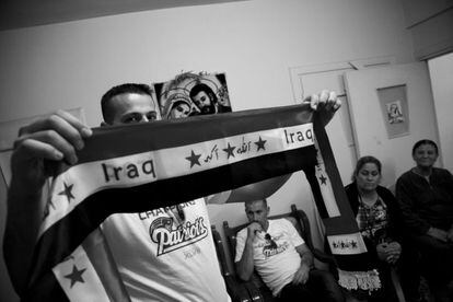 Danny Qas muestra una bufanda con la bandera de su país mientras le observa parte de su familia al fondo.