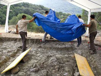 Voluntarios retiran una lona que cubre los restos de una de las fosas