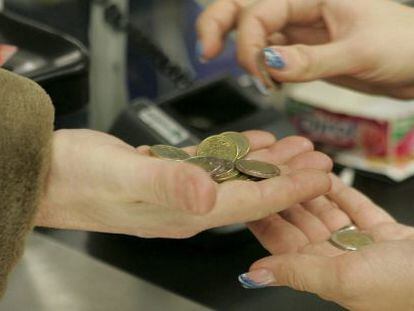 Una cajera ayuda a un cliente a contar las monedas de euro en un supermercado.