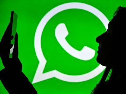 Una mujer sostiene un teléfono móvil ante un logo de WhatsApp, en enero de 2021, en Edmonton, Canadá.