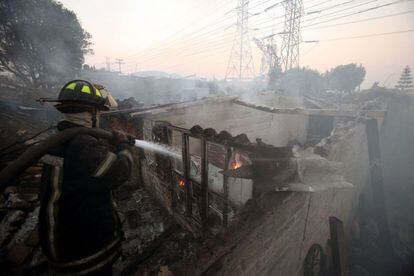 Un bombero apaga las llamas de una vivienda afectada por la explosión de un camión en el municipio de Ecatepec, al norte de México DF. La deflagración ha afectado una quincena de vehículos y una veintena de viviendas.