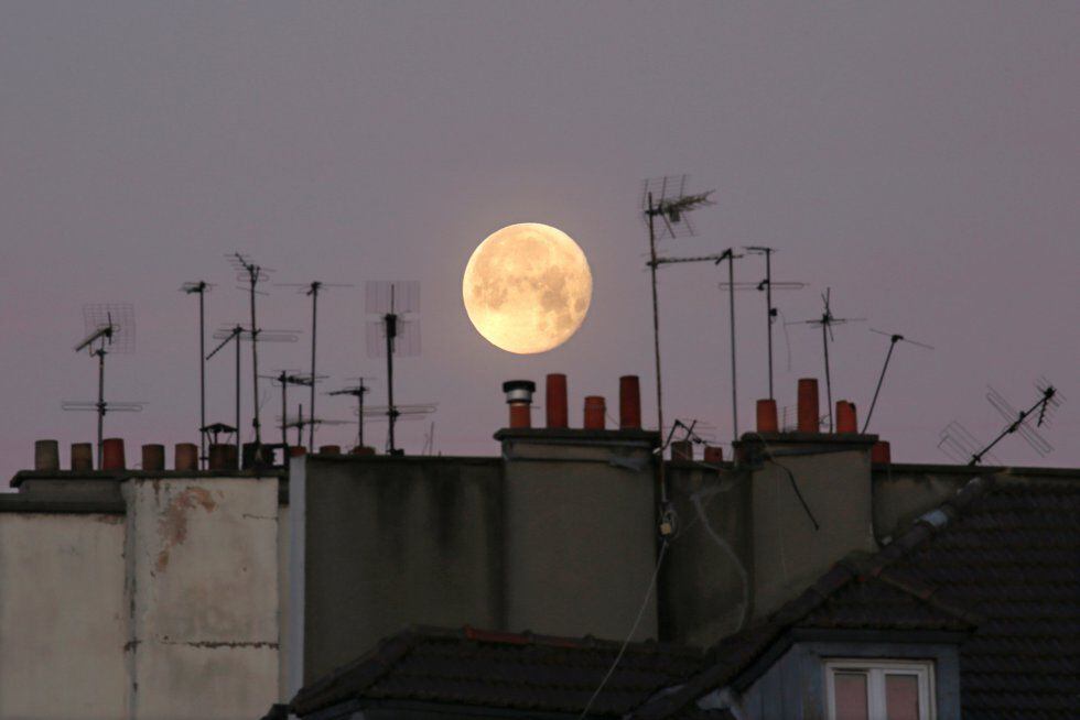 La Luna es vista tras chimeneas y antenas de televisión, en París (Francia).